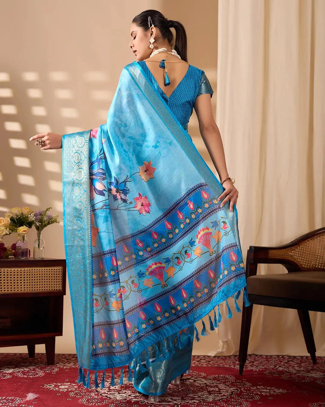 Woman wearing a blue saree with floral patterns in a room setting.
